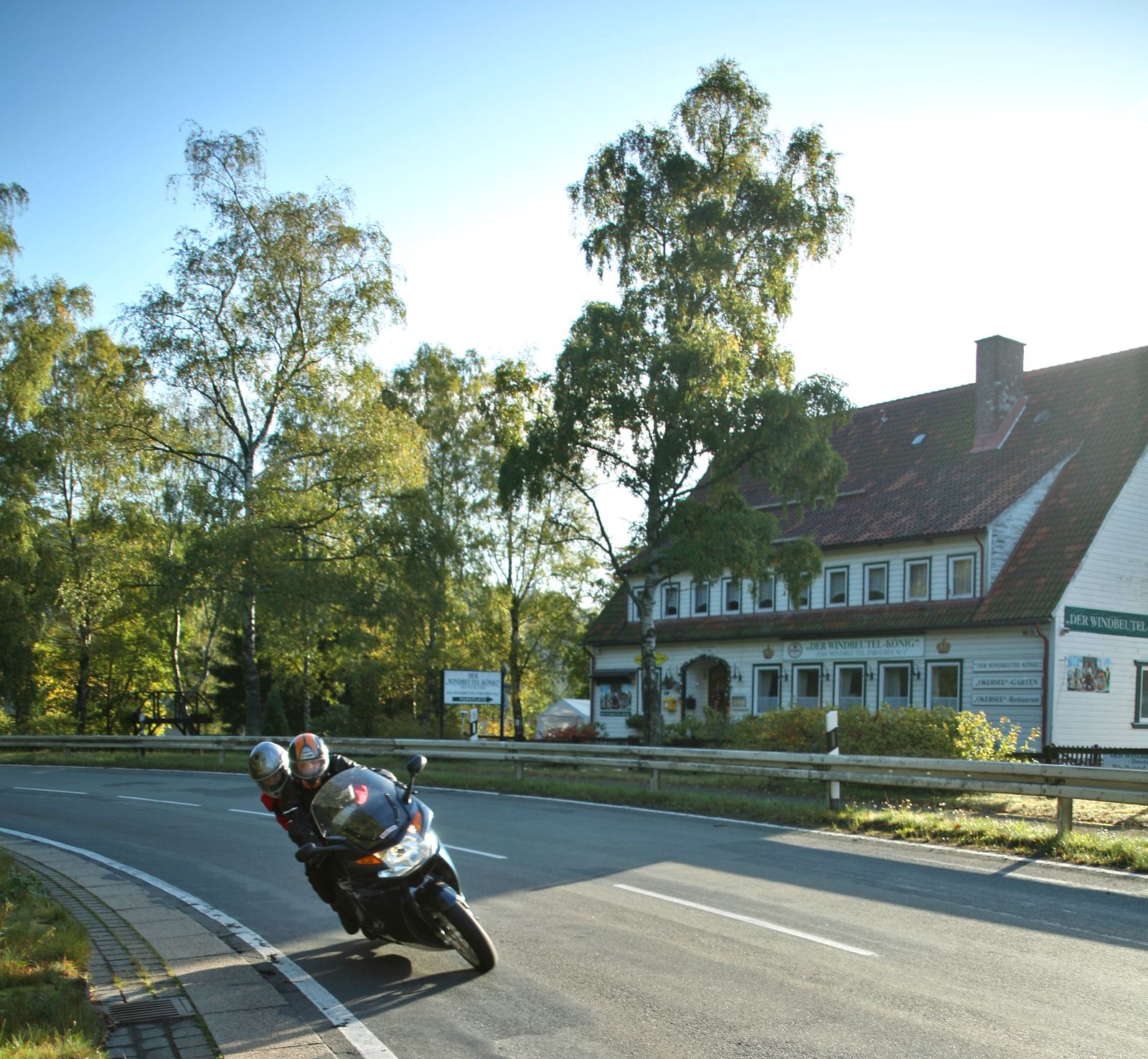 Gasthaus an einer Landstraße mit dem Schild Der Windbeutel-König, davor ein Motorrad in Schräglage